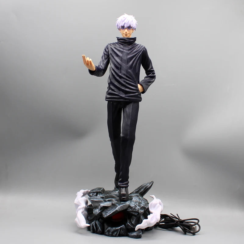 Figurine Gojo Satoru en tenue noire, main ouverte, sur socle rocheux avec câble.