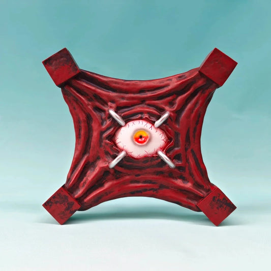 Figurine Œil Maudit rouge avec œil orange, orbite blanche et quatre poignées carrées.