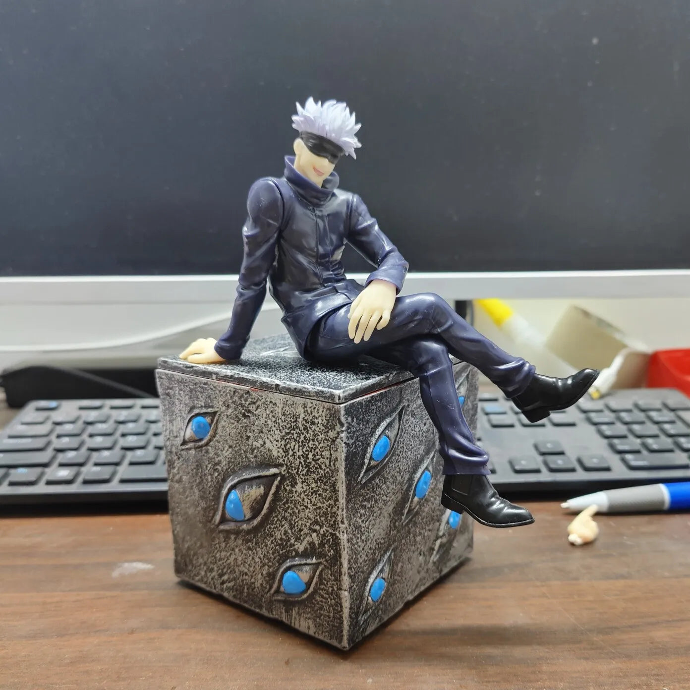Figurine en tenue noire assise sur cube boîte Prison aux yeux bleus