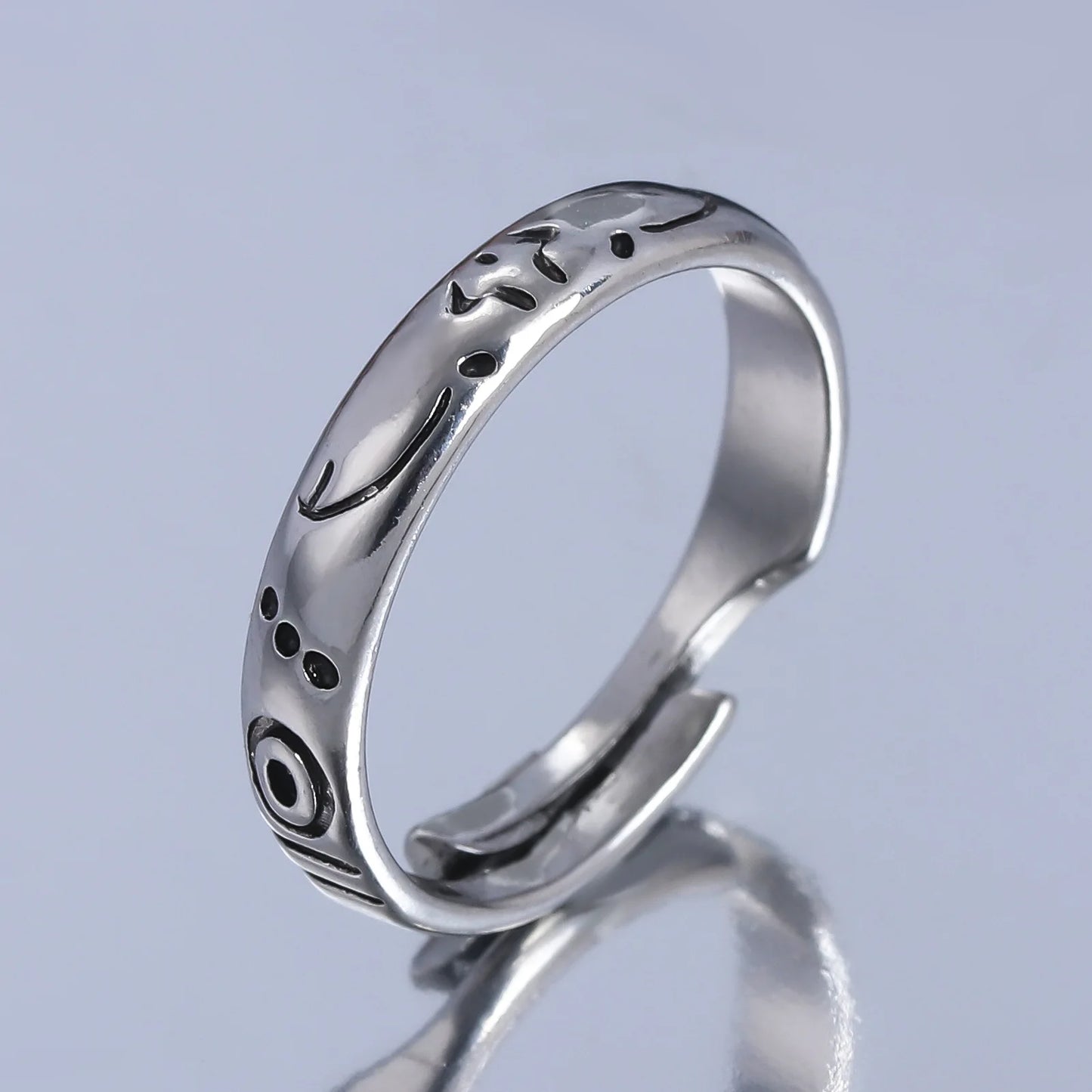 Bague argentée à bords lisses, décor noir et motifs gravés sur l’anneau.