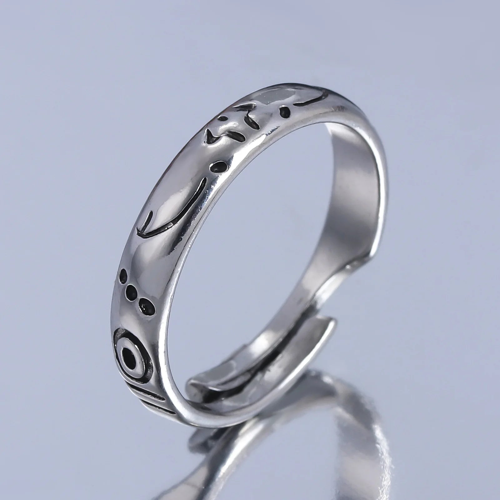 Bague argentée à bords lisses, décor noir et motifs gravés sur l’anneau.