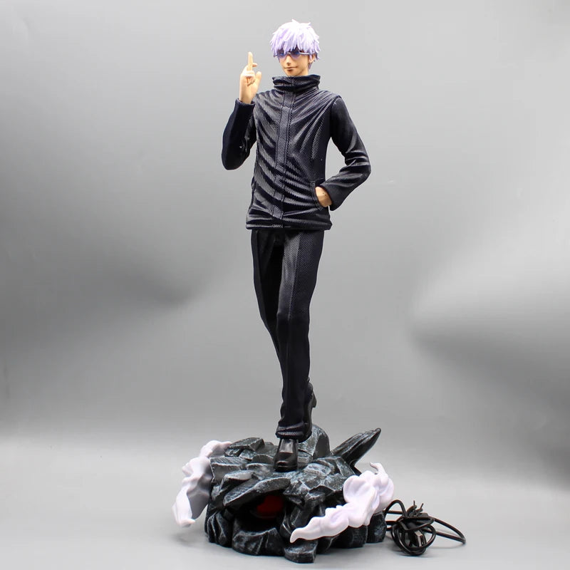 Figurine Gojo Satoru face, doigt levé, tenue noire sur socle rocheux lumineux.