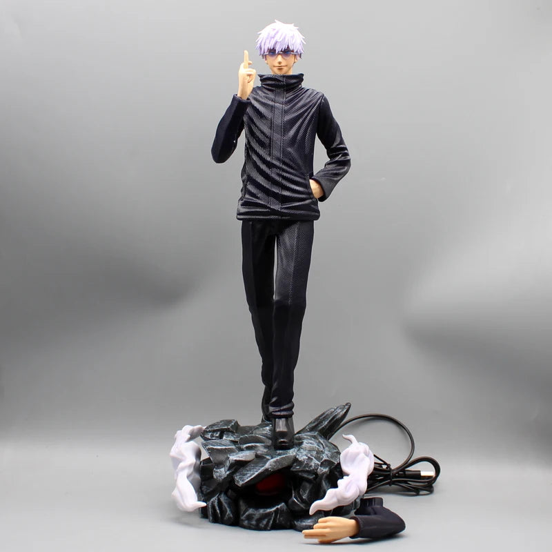 Figurine Gojo Satoru en tenue noire, doigt levé, sur socle rocheux et câble.